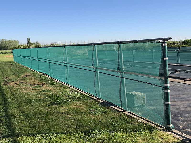 Green windbreak net installed along an outdoor boundary to reduce wind speed