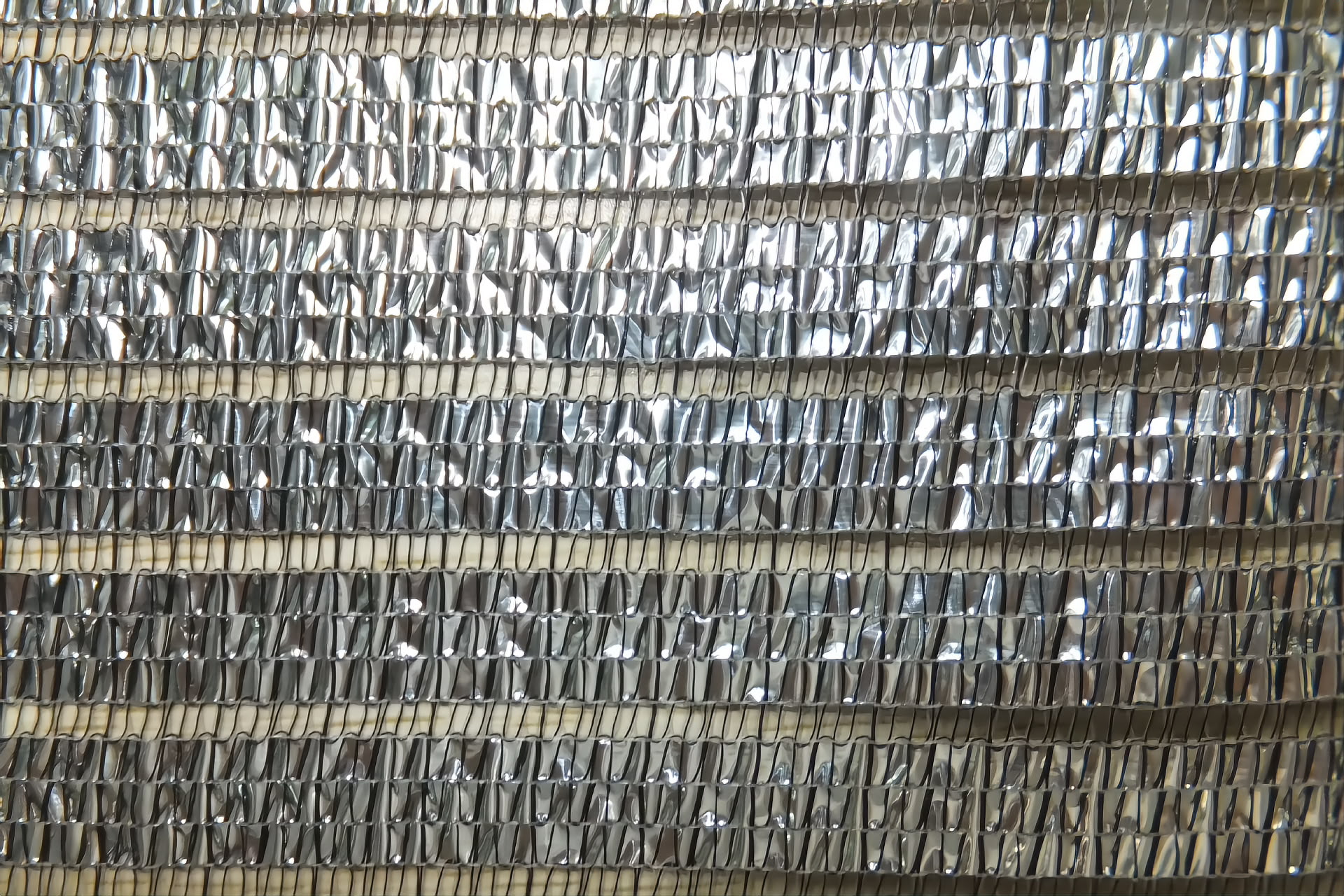 Primeiro plano de tela de sombra p&eacute;rola aluminizada mostrando a textura das fitas de HDPE tricotadas e o brilho met&aacute;lico